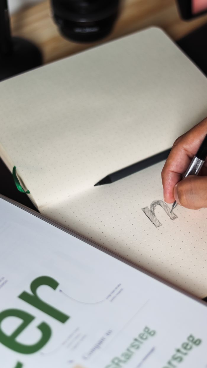 about-us-01 A person writing in a notebook, focusing on pencil sketching and typography design.